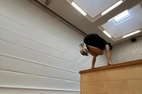 Turner führt einen Handstand über eine Holzkastenbank in einer Sporthalle mit Oberlichtern durch.
